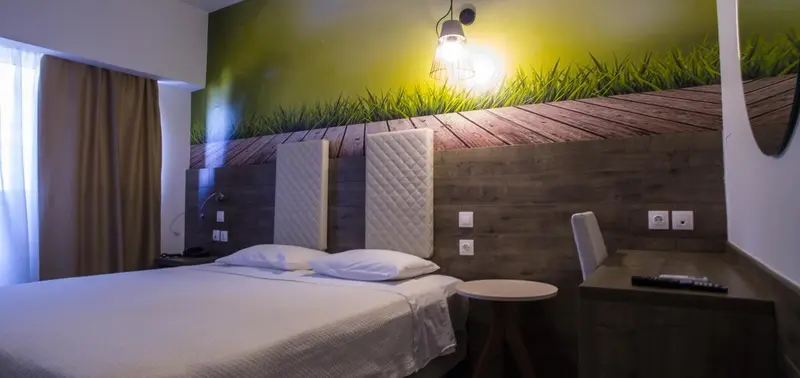 Chambre lumineuse avec un lit double et un décor mural représentant un paysage.