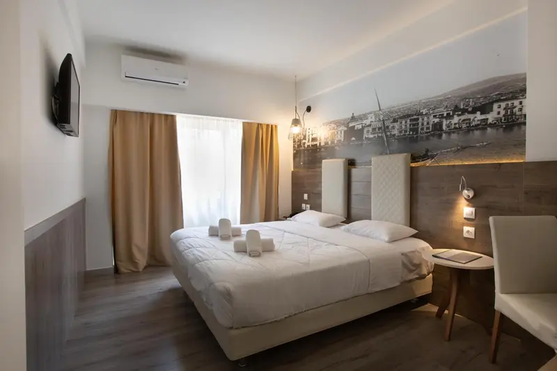 Une chambre lumineuse avec un grand lit et un décor mural représentant une ville.