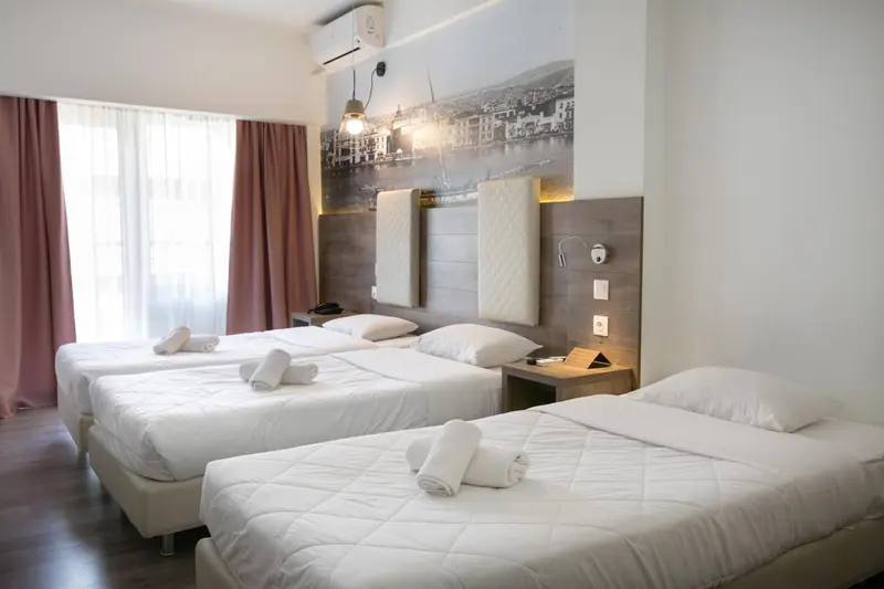 Chambre avec trois lits simples et une décoration murale représentant un paysage urbain.