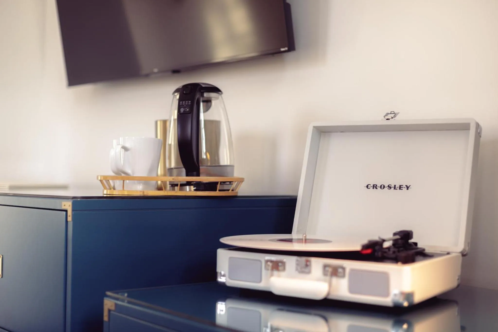 Une cafetière et un tourne-disque reposent sur une commode sombre.