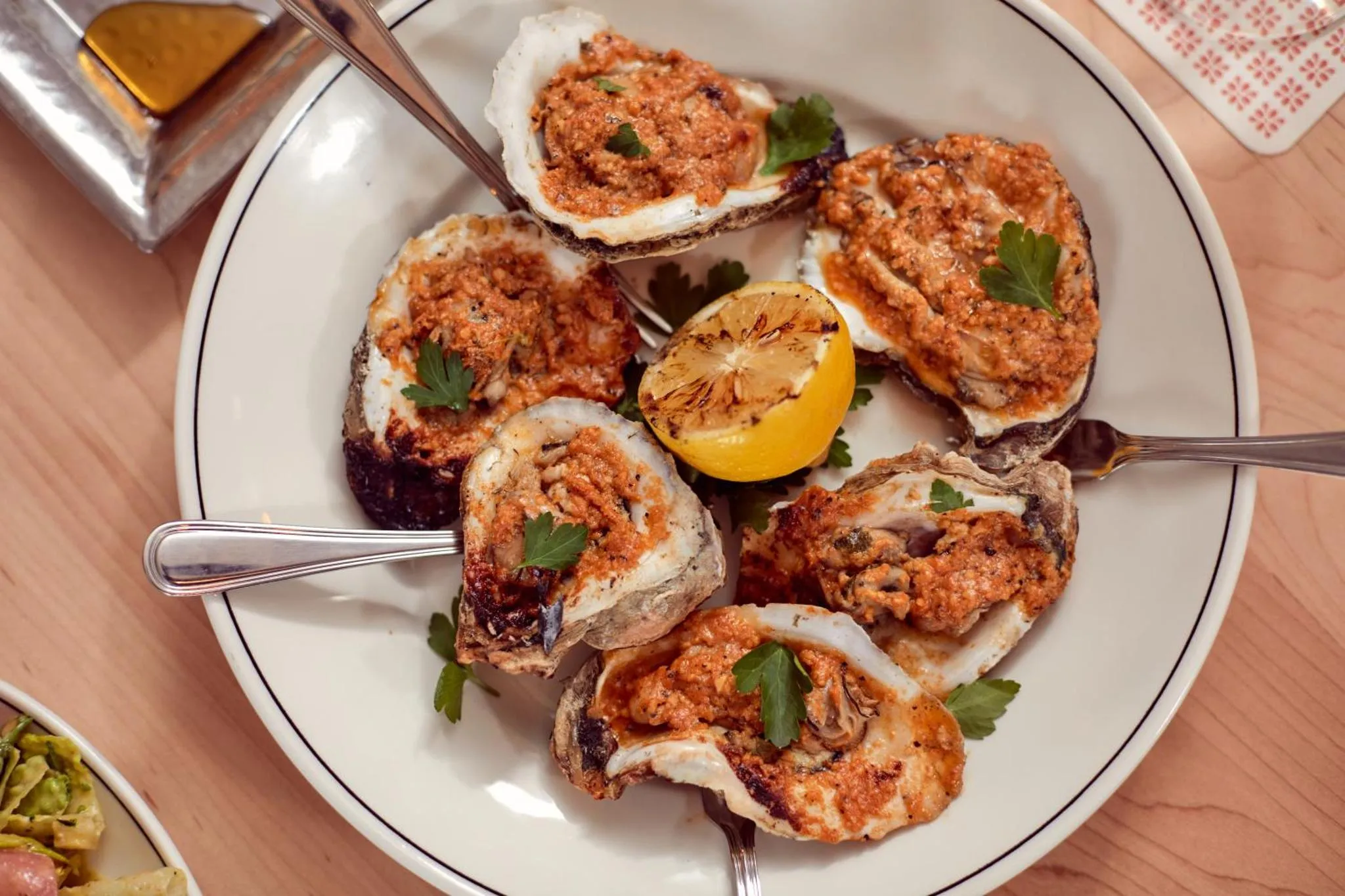 Assiette d'huîtres gratinées garnies de persil et accompagnées d'une tranche de citron.