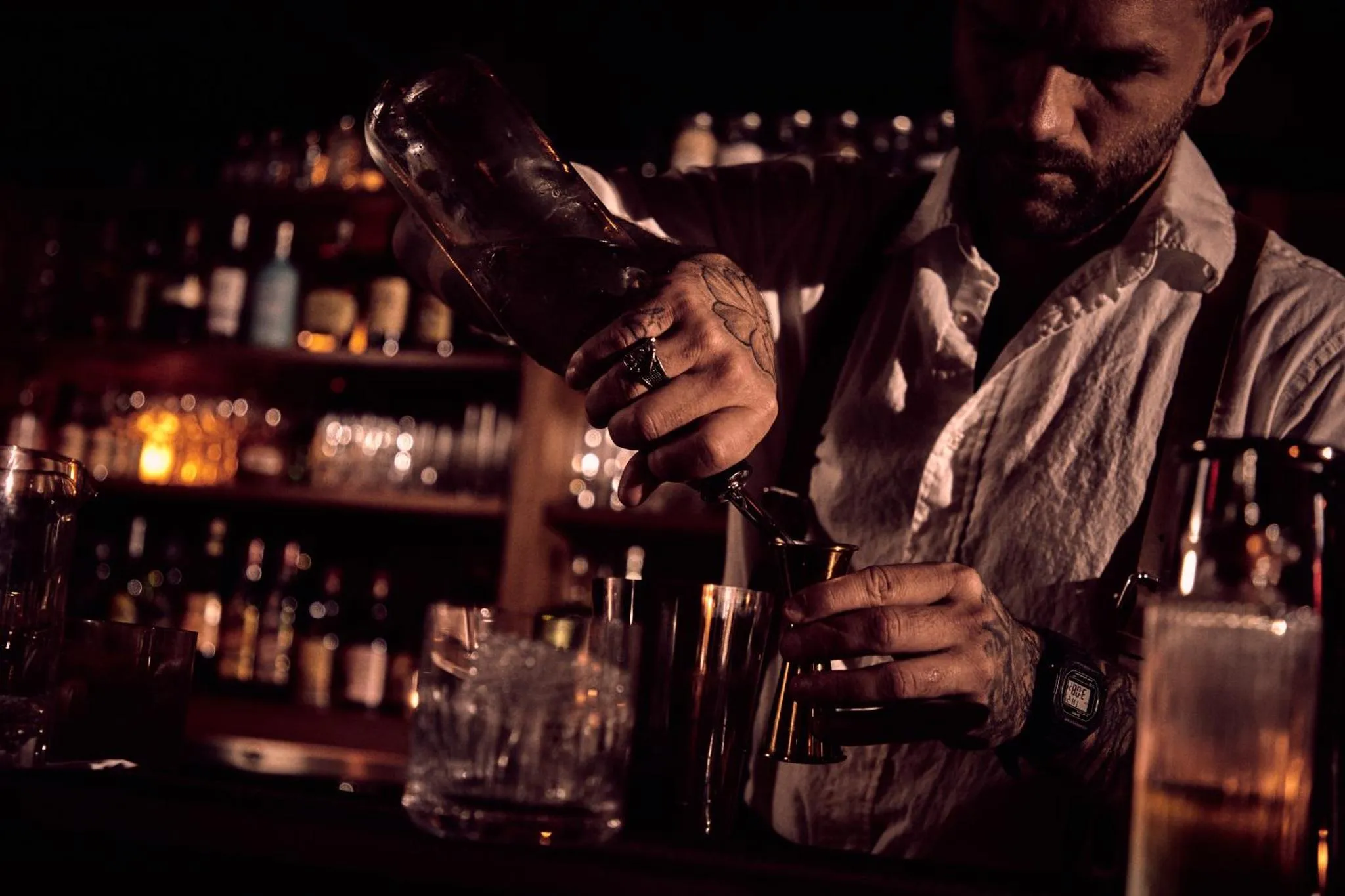 Un barman prépare un cocktail derrière un comptoir illuminé.