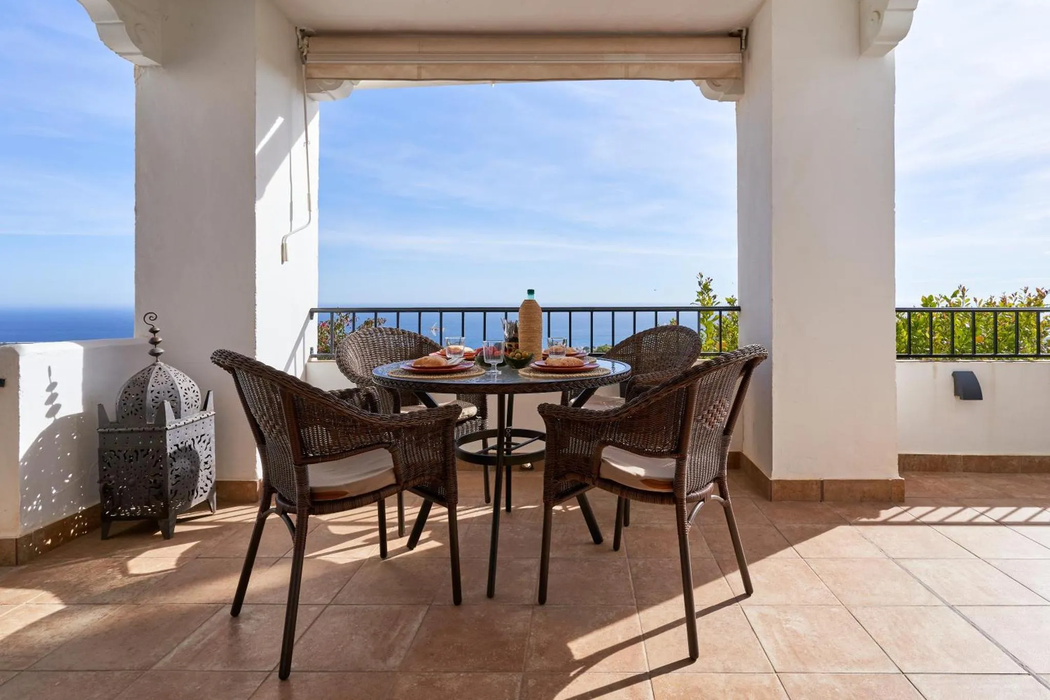 Une table ronde en osier avec des chaises sur une terrasse carrelée offre une vue sur la mer.