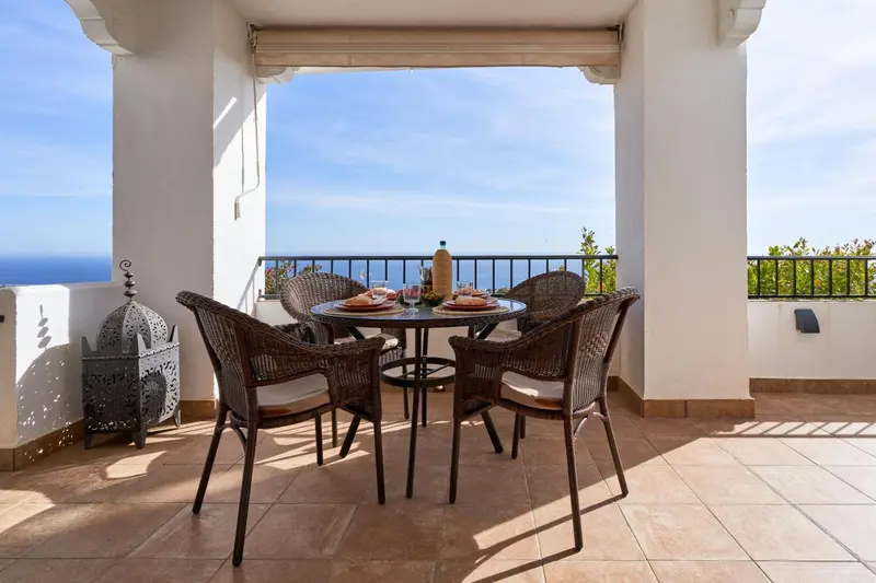 Une table ronde en osier avec des chaises sur une terrasse carrelée offre une vue sur la mer.
