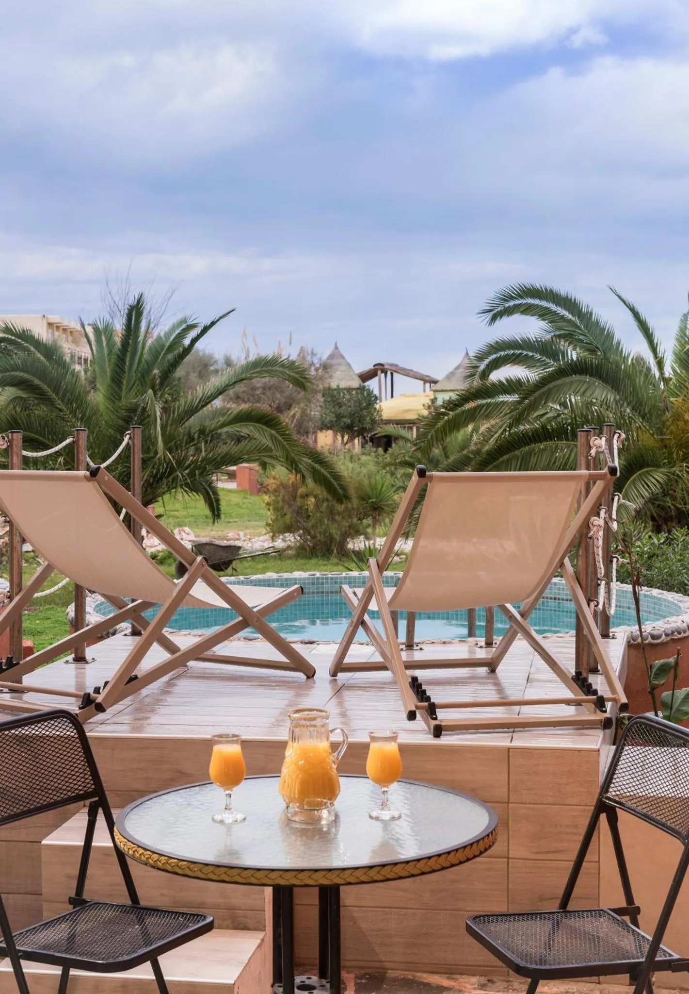 Deux transats et une table basse avec des boissons sont disposés au bord d'une piscine.