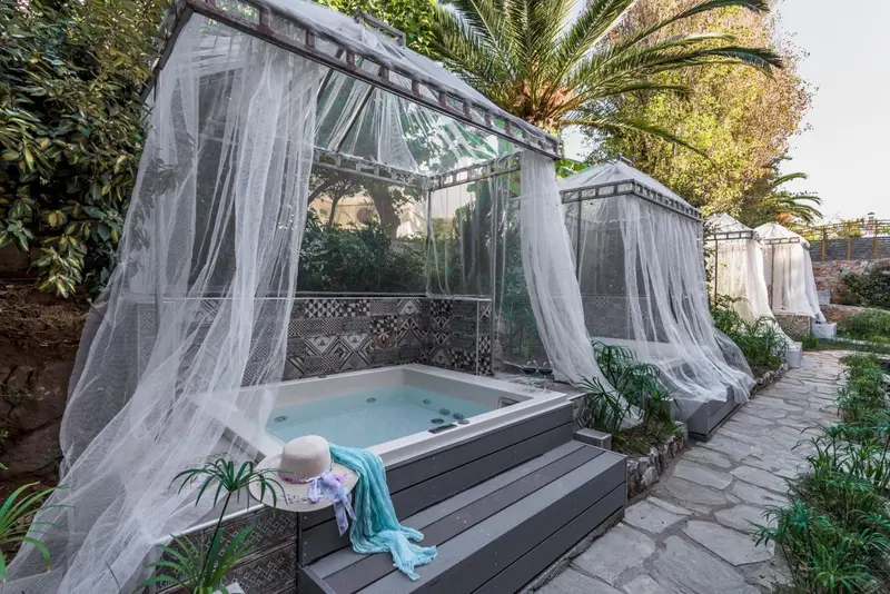 Jacuzzi extérieur entouré de moustiquaires et de végétation luxuriante.