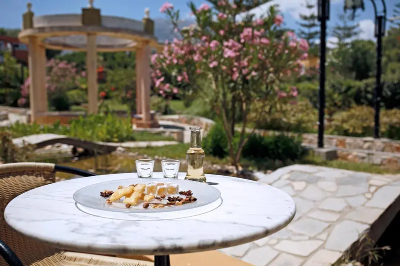 Une table ronde en marbre présente des boissons et des pâtisseries dans un jardin fleuri.