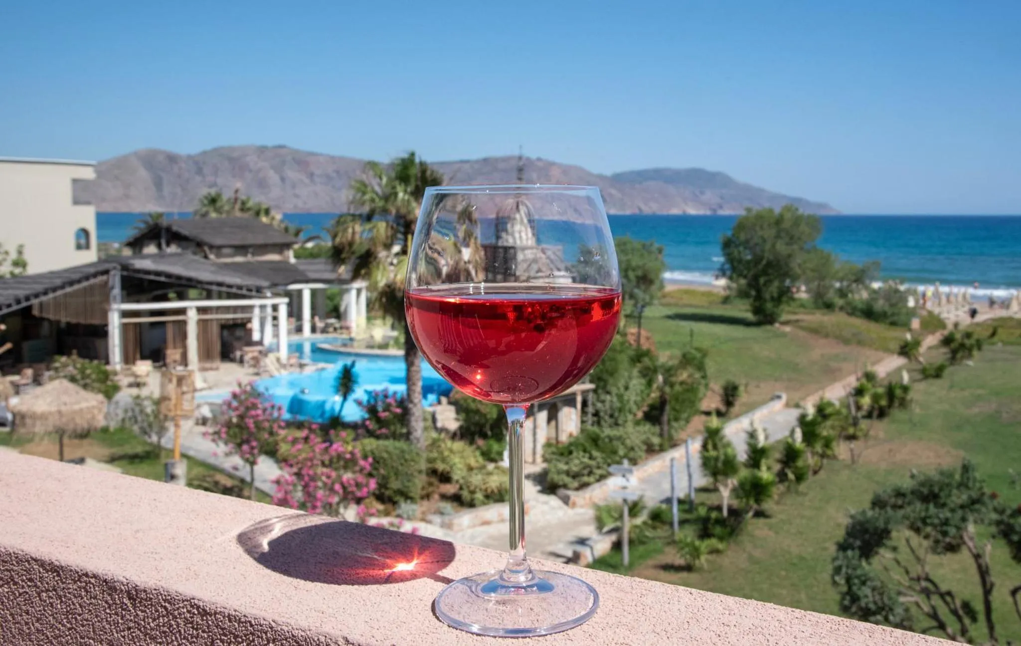 Un verre de vin rosé est posé sur une balustrade avec vue sur la mer et les montagnes.