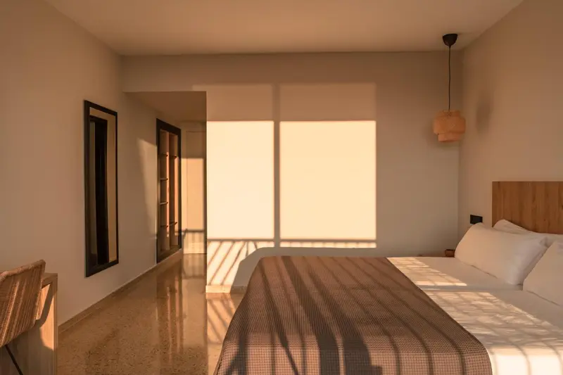 Une chambre lumineuse avec un lit fait et une lumière naturelle filtrant à travers les stores.