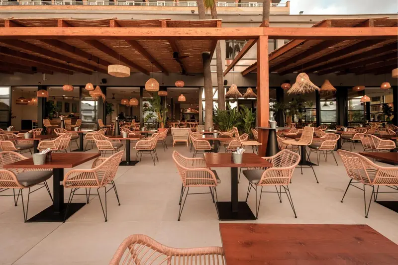 Une salle à manger extérieure avec des tables et des chaises en rotin sous une pergola en bois.