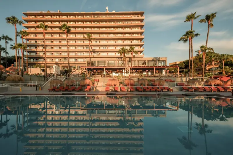 Bâtiment beige à plusieurs étages reflété dans une piscine au bord de la mer.
