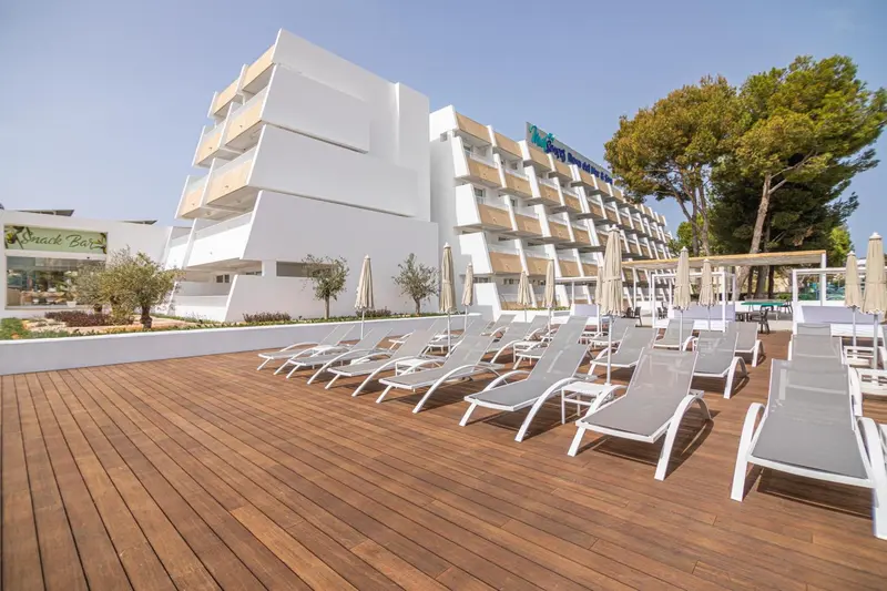Terrasse en bois avec transats blancs devant un bâtiment blanc.