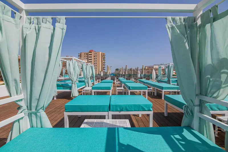 Terrasse aménagée avec des transats turquoise sous des rideaux légers.