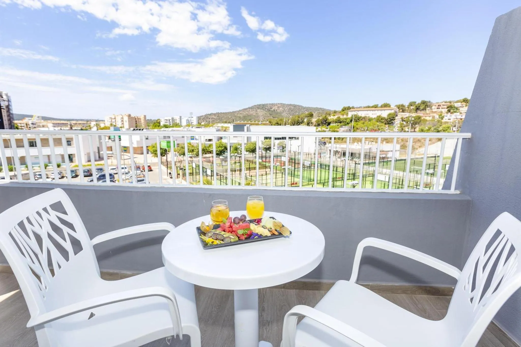 Une table basse avec des fruits et des boissons sur une terrasse ensoleillée avec vue sur le paysage.
