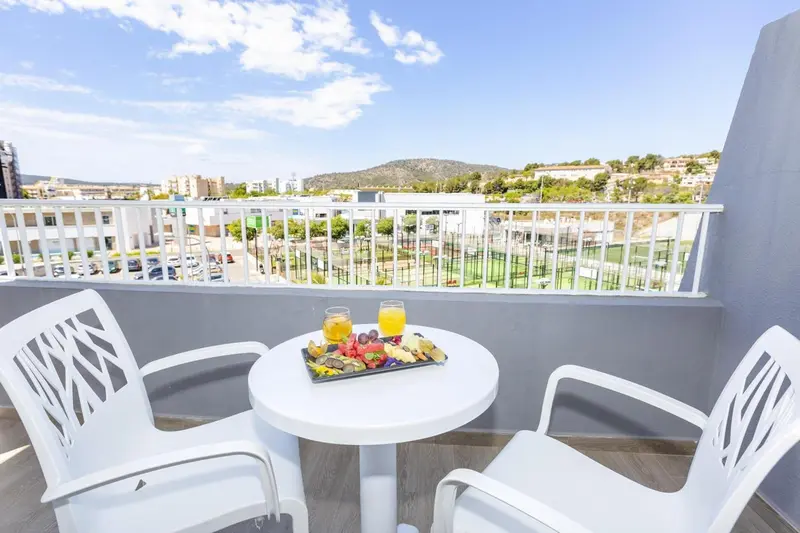 Une table basse avec des fruits et des boissons sur une terrasse ensoleillée avec vue sur le paysage.