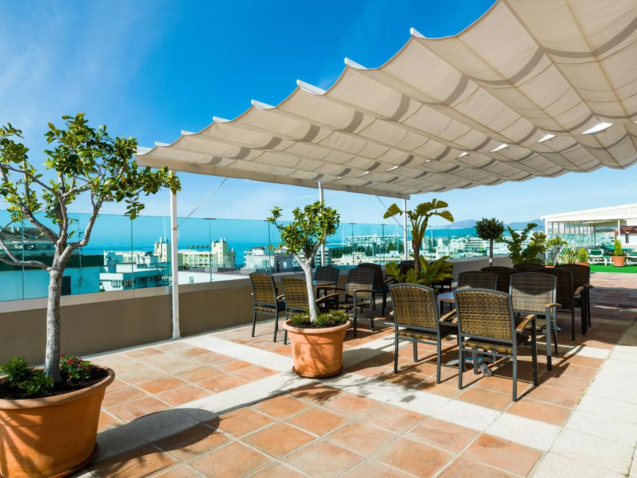 Terrasse ombragée avec mobilier de jardin et vue sur la mer.