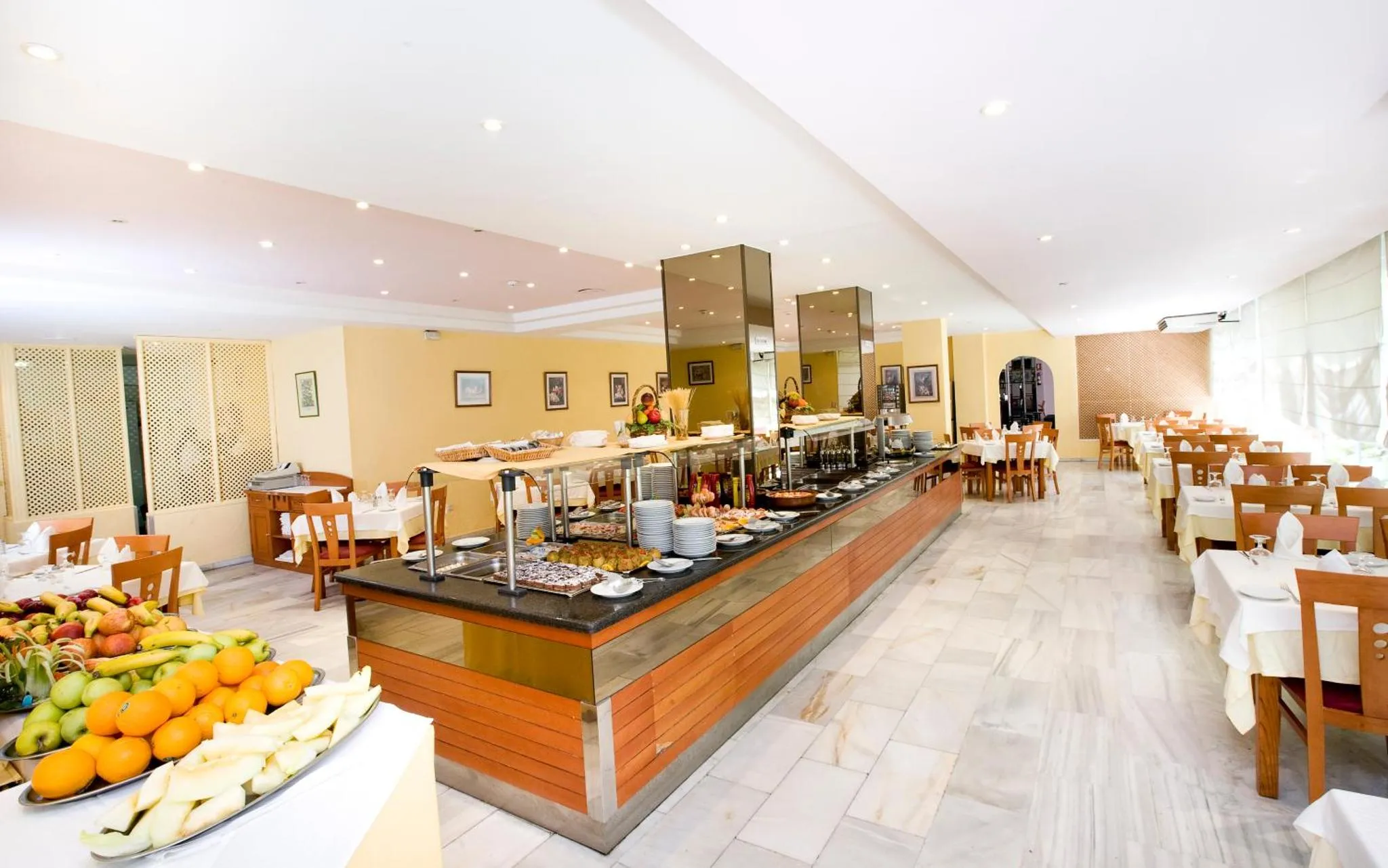 Une salle lumineuse présente un buffet garni de plats variés et de fruits frais.