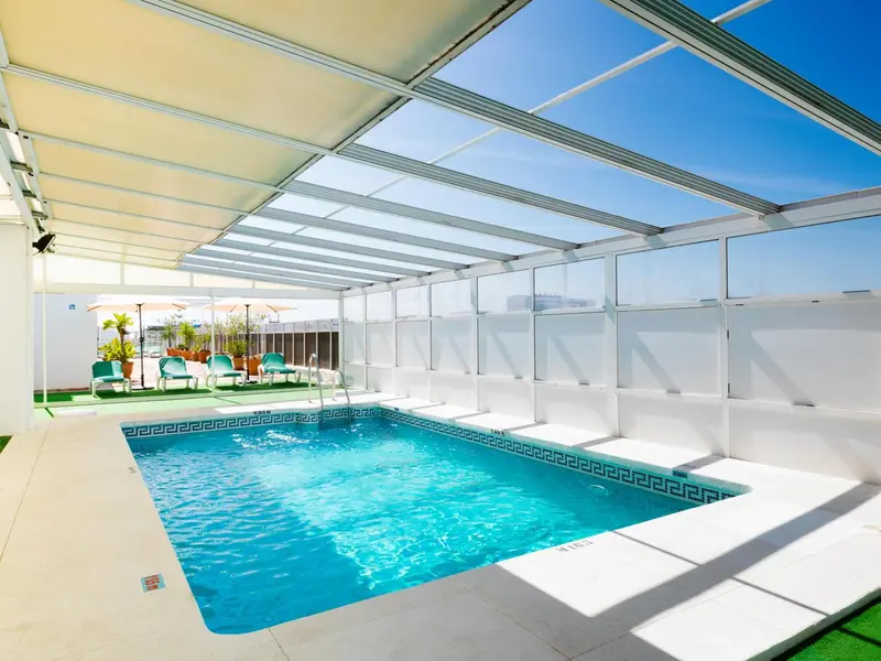Une piscine rectangulaire avec des transats et une structure de toit en verre.