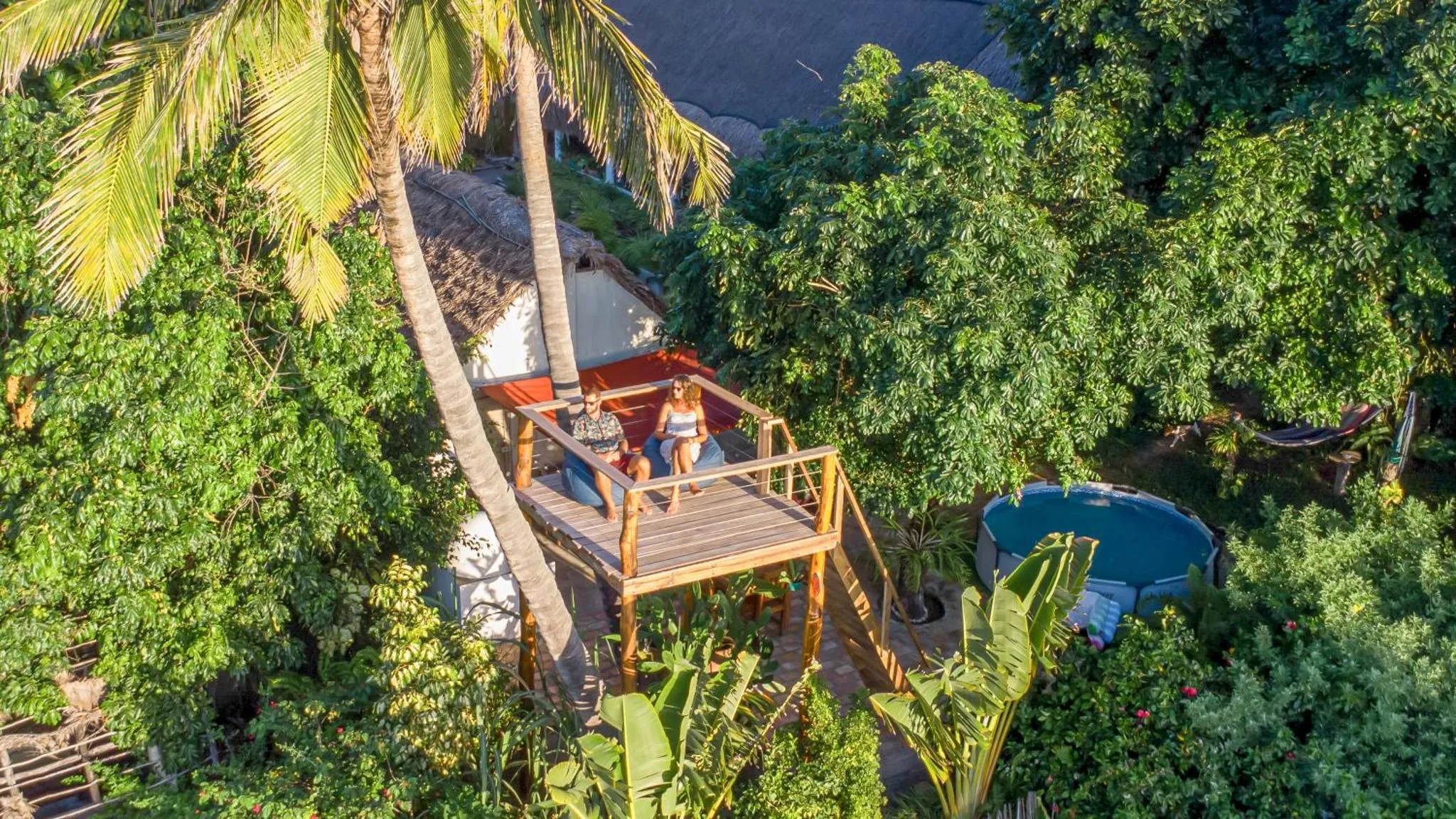 Terrasse en bois sur pilotis avec deux personnes assises et une piscine hors sol.