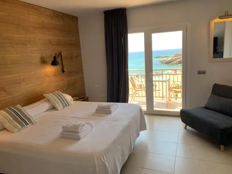 Une chambre lumineuse avec un lit fait et un accès à un balcon avec vue sur la mer.