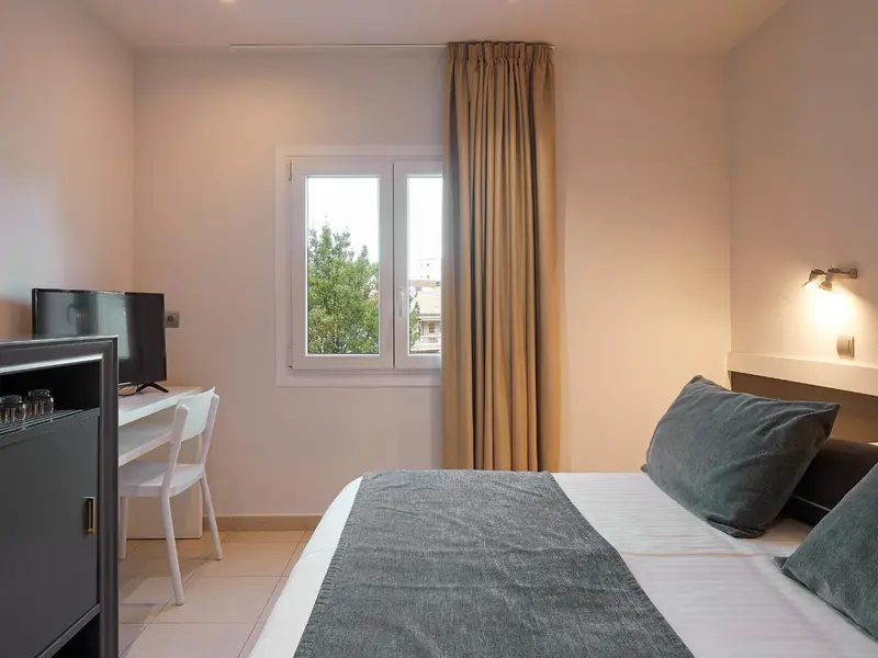 Une chambre lumineuse avec un lit fait et un bureau près de la fenêtre.