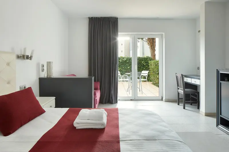 Une chambre lumineuse avec un lit rouge et un bureau près d'une terrasse.