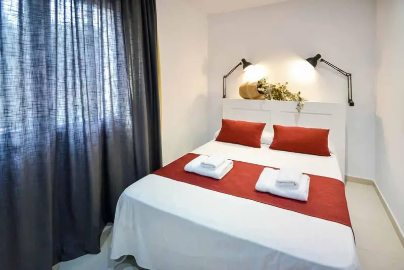 Une chambre lumineuse avec un grand lit recouvert d'une courtepointe rouge et de coussins.