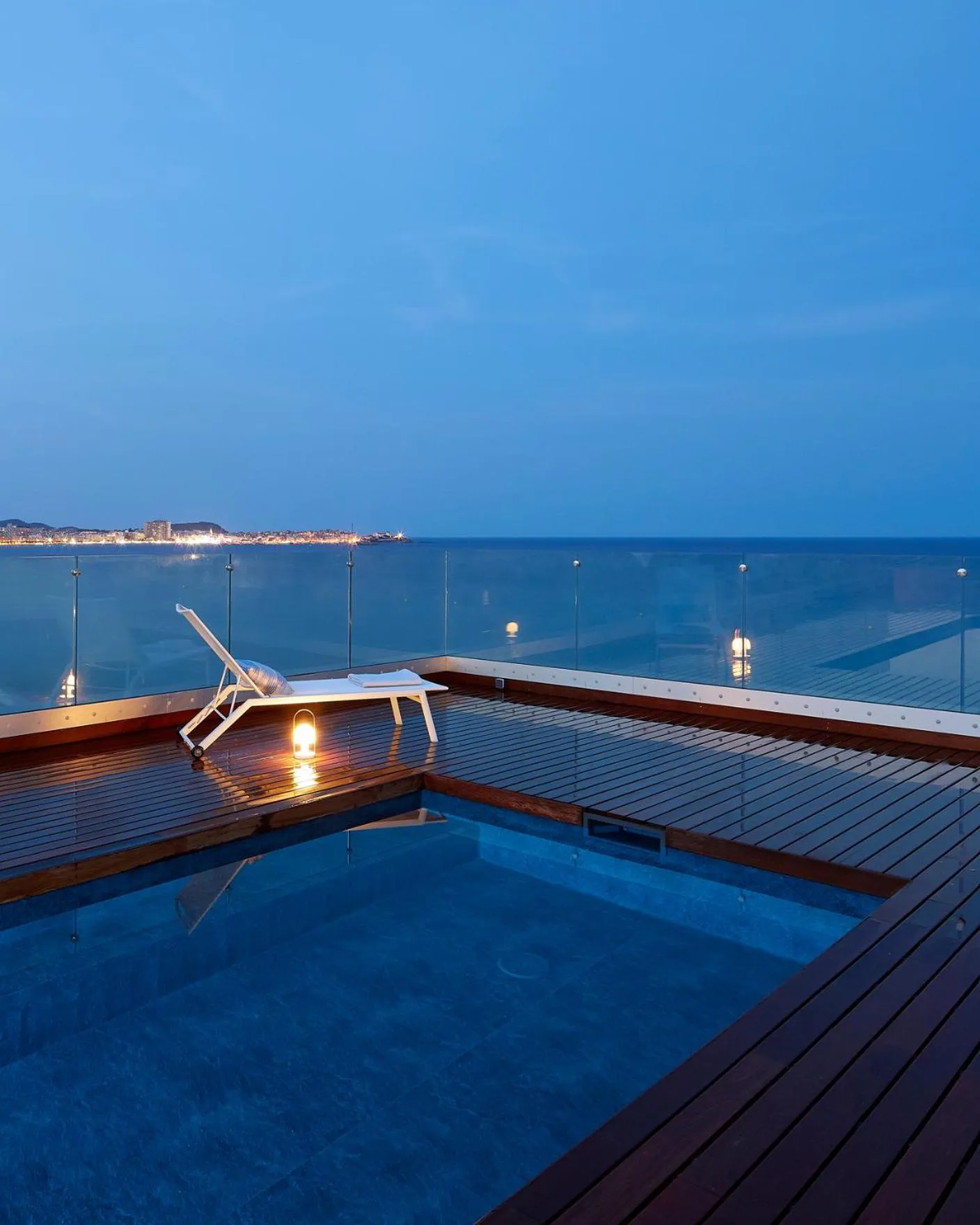 Terrasse en bois avec piscine et vue sur la mer au crépuscule.