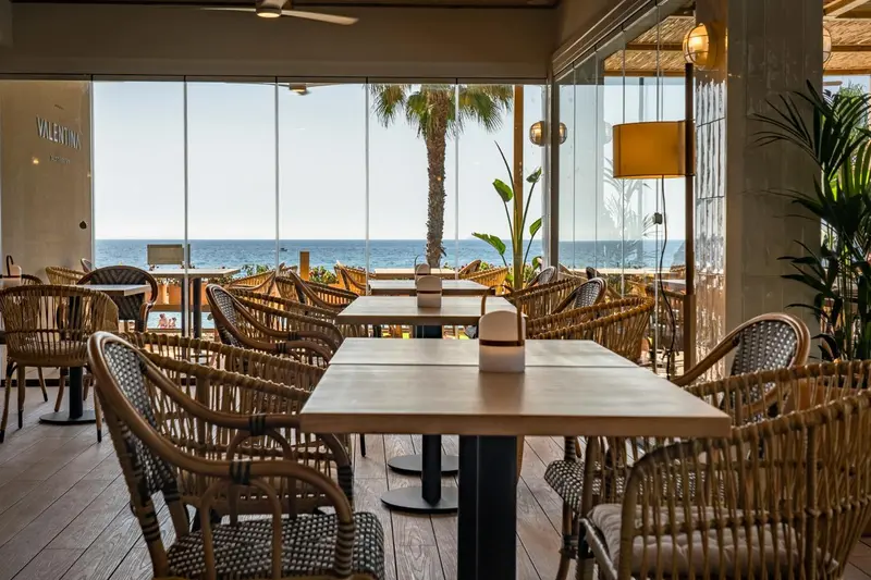 Une salle à manger lumineuse avec des tables et des chaises en rotin donnant sur la mer.