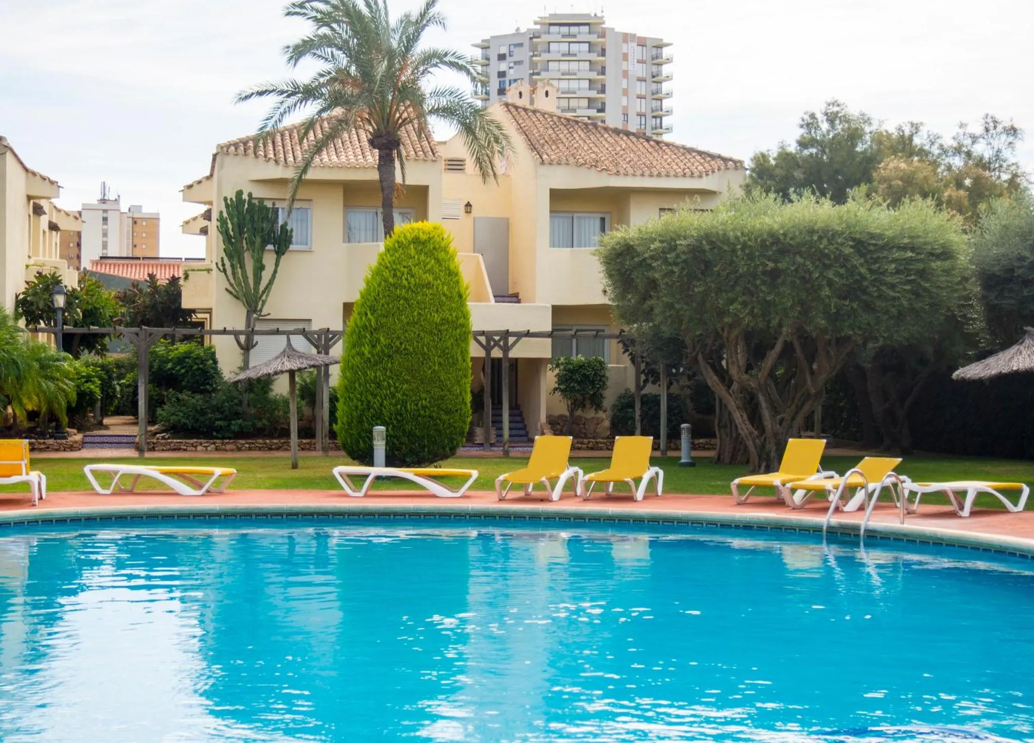 Vue d'une piscine avec des transats et un bâtiment jaune en arrière-plan.