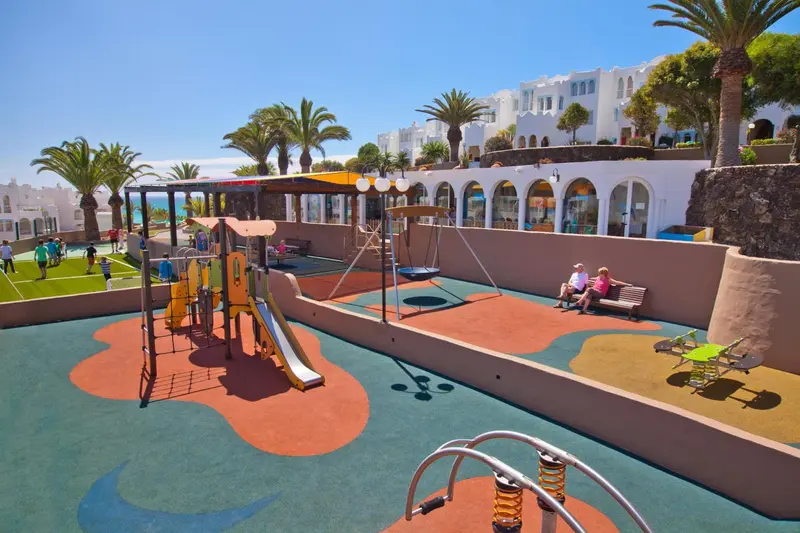 Aire de jeux colorée avec des enfants et des adultes assis sur une terrasse.