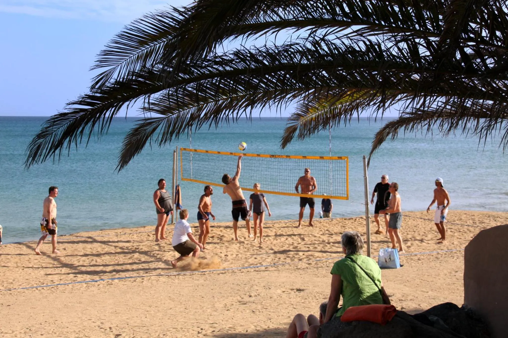 Des personnes jouent au volley-ball sur une plage de sable fin face à la mer.
