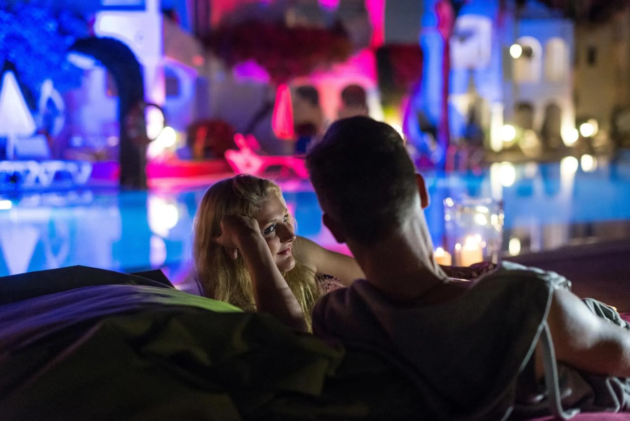 Un couple se détend au bord d'une piscine illuminée la nuit.