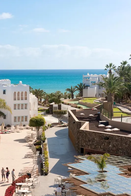 Vue aérienne d'un complexe hôtelier blanc avec piscine et végétation tropicale face à la mer.