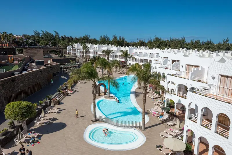 Vue aérienne d'un complexe hôtelier blanc avec des piscines et des palmiers.