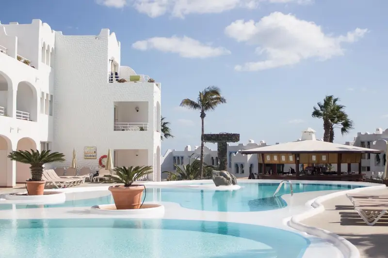 Vue d'une piscine turquoise bordée de transats devant un bâtiment blanc.