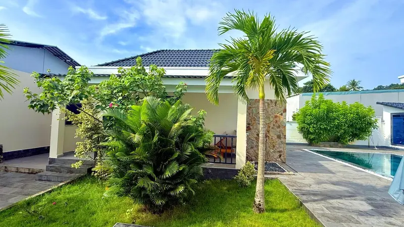 Petite maison blanche avec végétation tropicale et piscine.