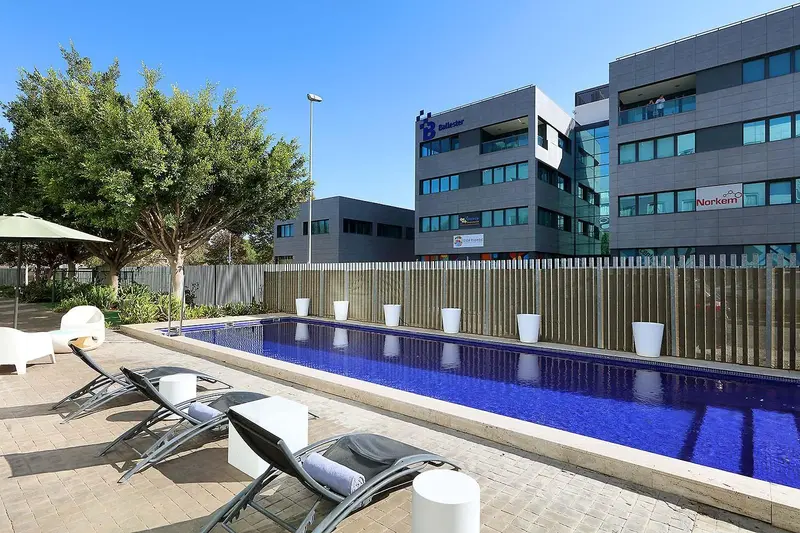 Transats blancs disposés autour d'une piscine rectangulaire bleu clair.