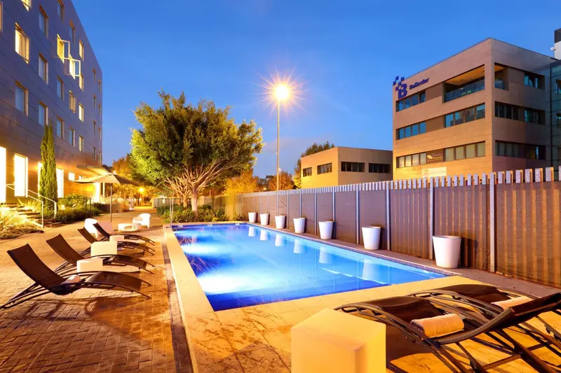 Piscine rectangulaire avec transats et végétation luxuriante au crépuscule.