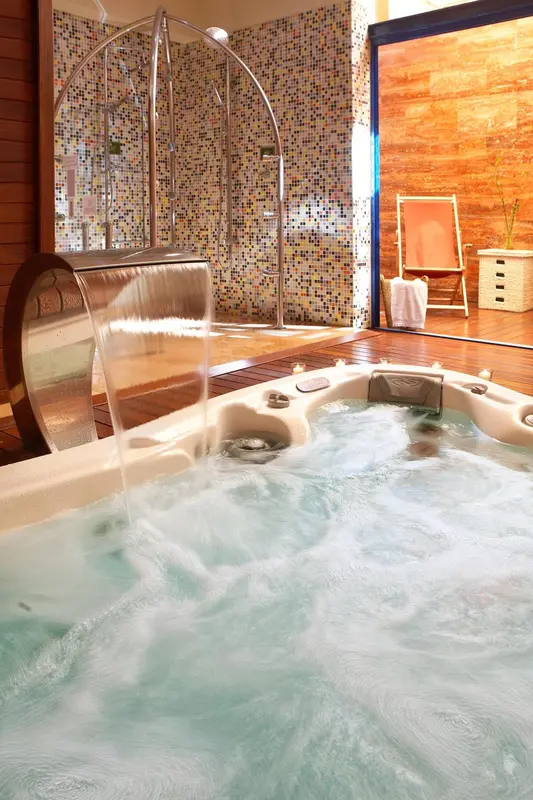 Un jacuzzi d'angle avec cascade dans une salle de bain lumineuse.