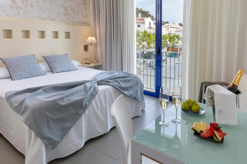 Une chambre lumineuse avec un grand lit et une table basse décorée de fruits et de champagne.