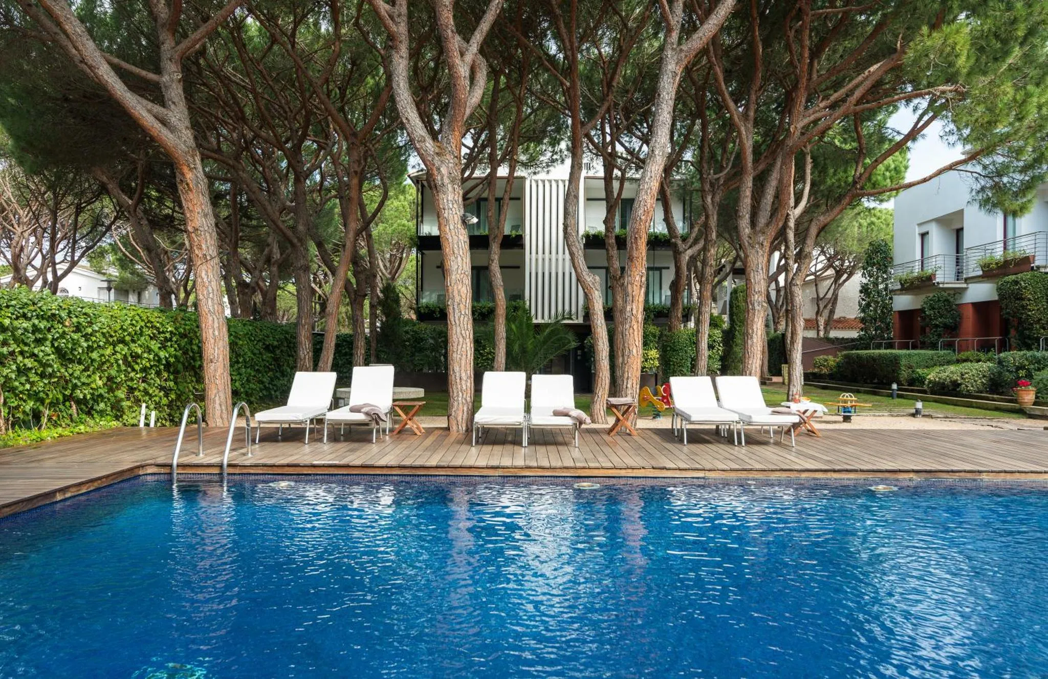 Transats blancs alignés sur une terrasse en bois au bord d'une piscine bleue.