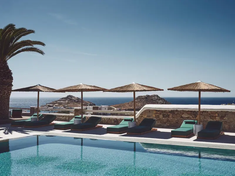 Transats verts disposés au bord d'une piscine turquoise avec vue sur la mer.