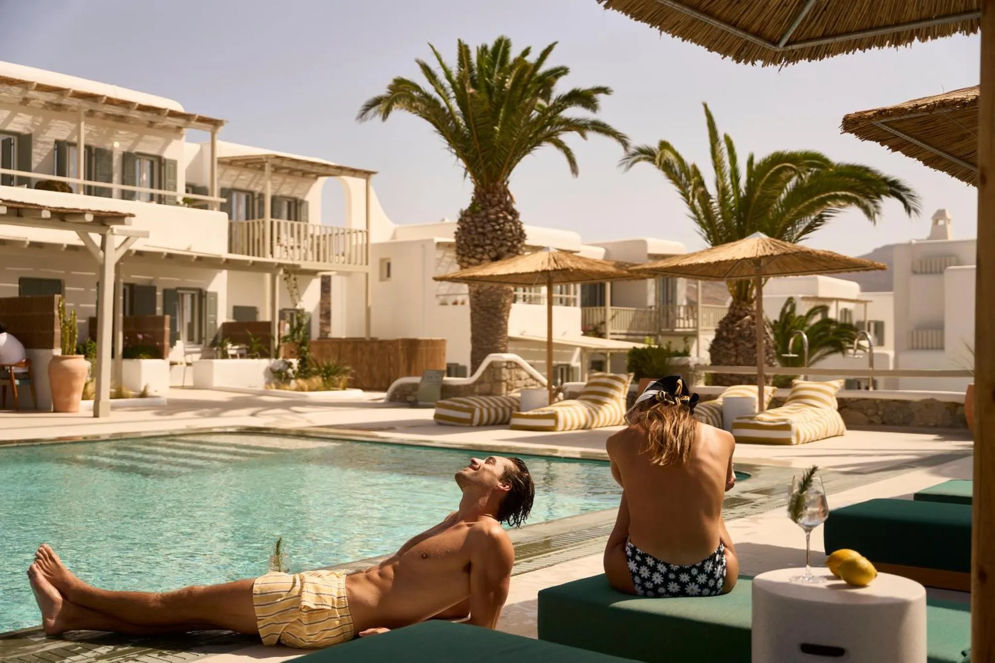 Des personnes se détendent au bord d'une piscine ensoleillée avec des palmiers en arrière-plan.