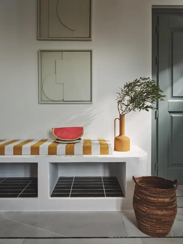 Une nature morte avec une pastèque et une plante sur une console rayée.