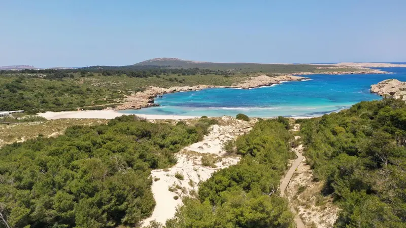 Vue aérienne d'une plage de sable fin bordée d'une eau turquoise et d'une végétation luxuriante.