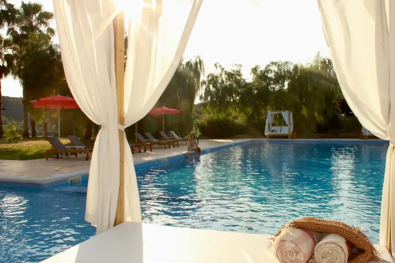 Vue sur une piscine ensoleillée depuis un espace détente ombragé.