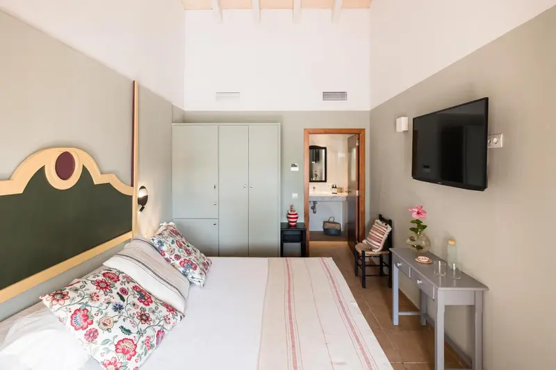 Une chambre lumineuse avec un lit recouvert de motifs floraux et un téléviseur mural.
