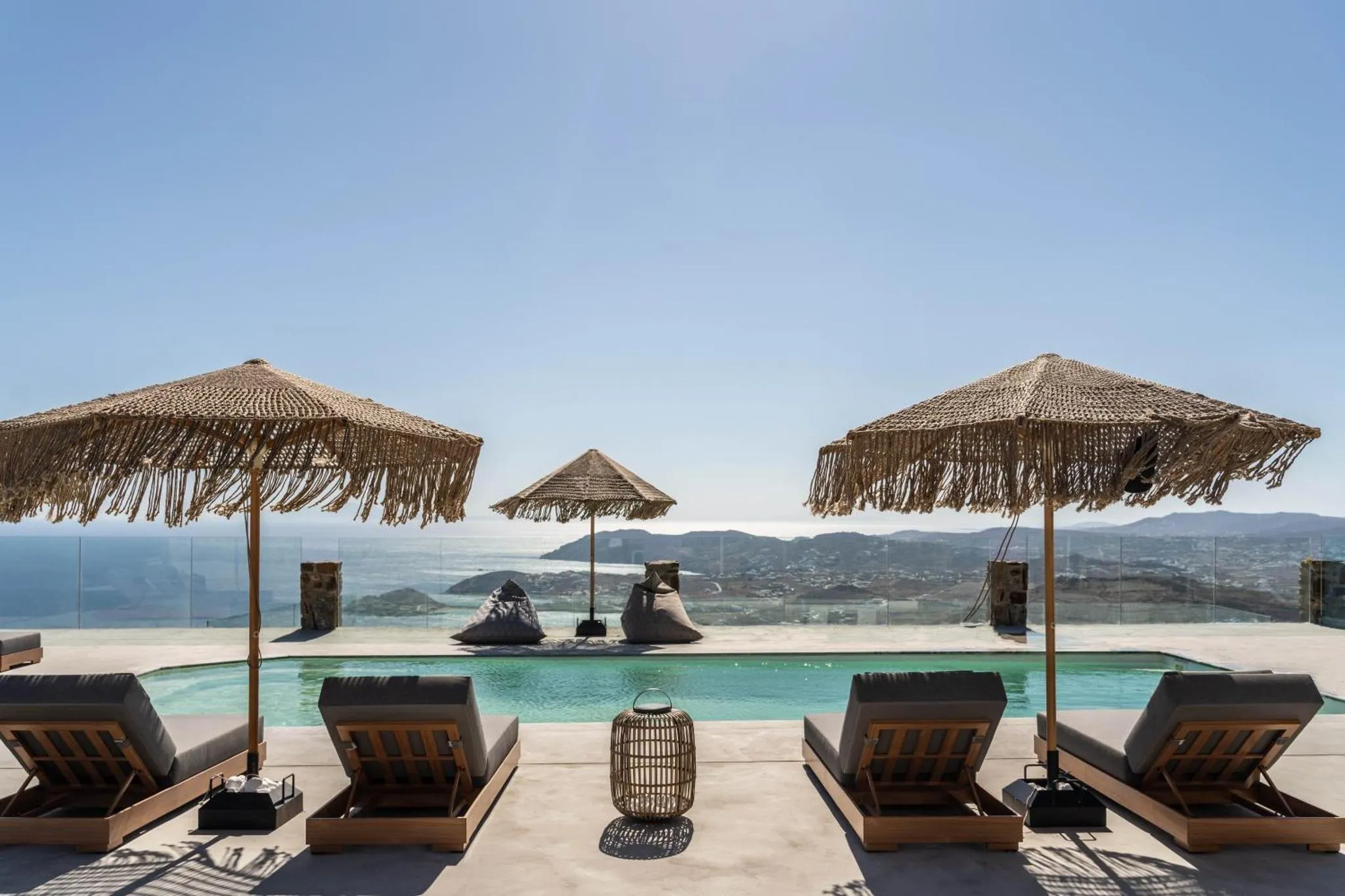 Transats et parasols à l'ombre bordent une piscine à débordement avec vue sur la mer.