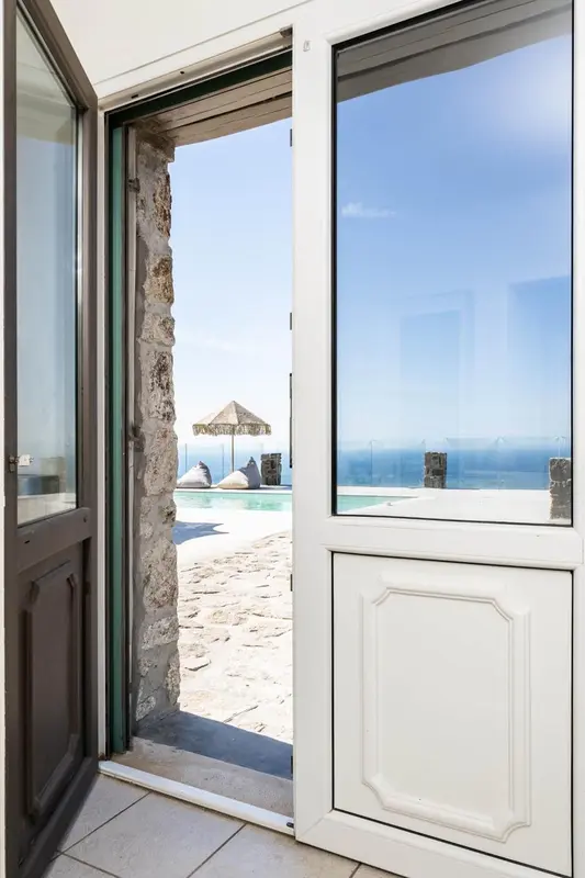 Une porte ouverte dévoile une vue sur une piscine et la mer.
